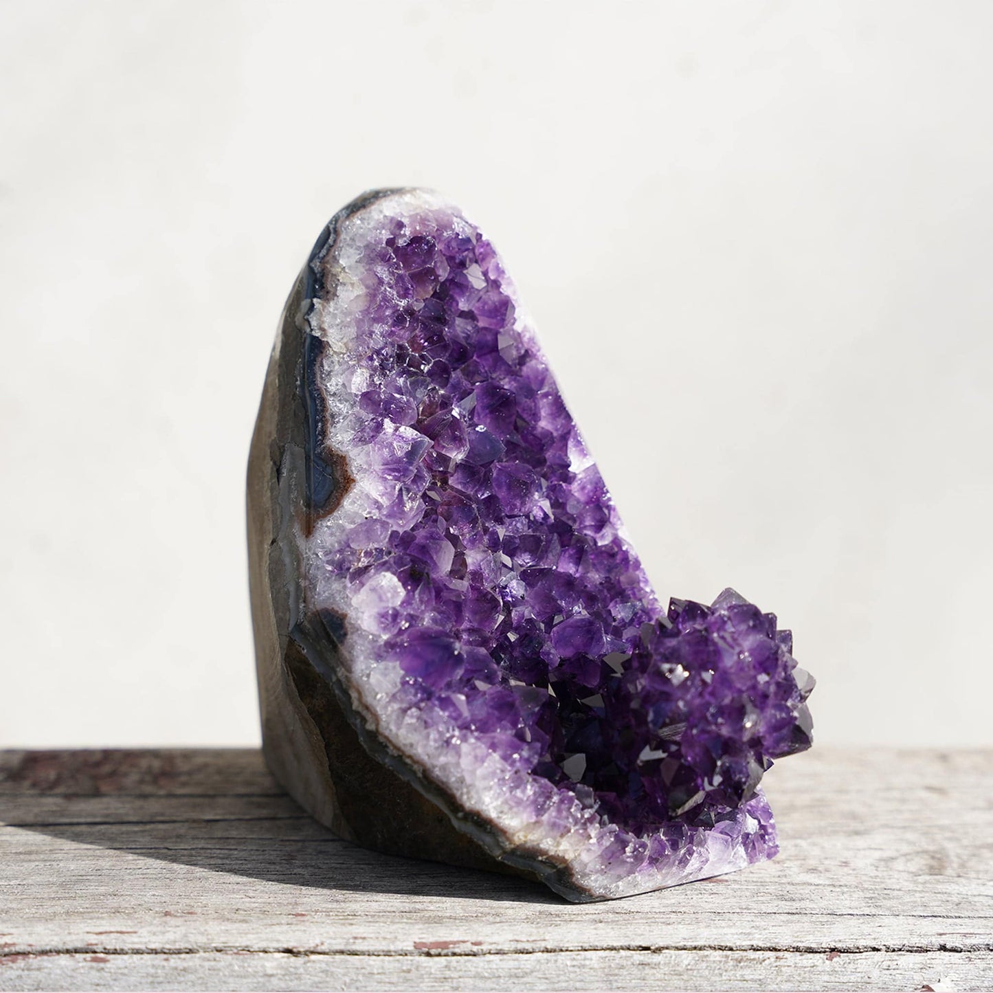 Stunning eye-catching natural formation on this gorgeous cut-base geode amethyst.  Bands of layered minerals including white quartz, blue agate, and green celadonite separate the raw basalt rock in the back from the glimmering front of deep purple crystal peaks.