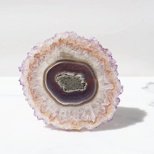 Eye-resembling mega-size Uruguayan amethyst stalactite slice. Transparent agate center and light-reflecting all across the piece to its pastel toned purple crystal peaks.