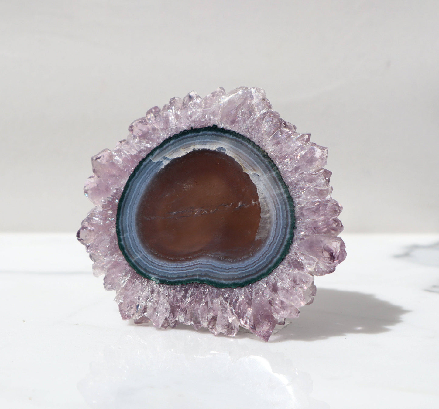 Grand stalactite slice. Flower-resembling formation, nature-made of hearth tone agate with bands of blue and green jasper. Bordering this glee is a thick and graceful layer of large lavender color quartz crystals.