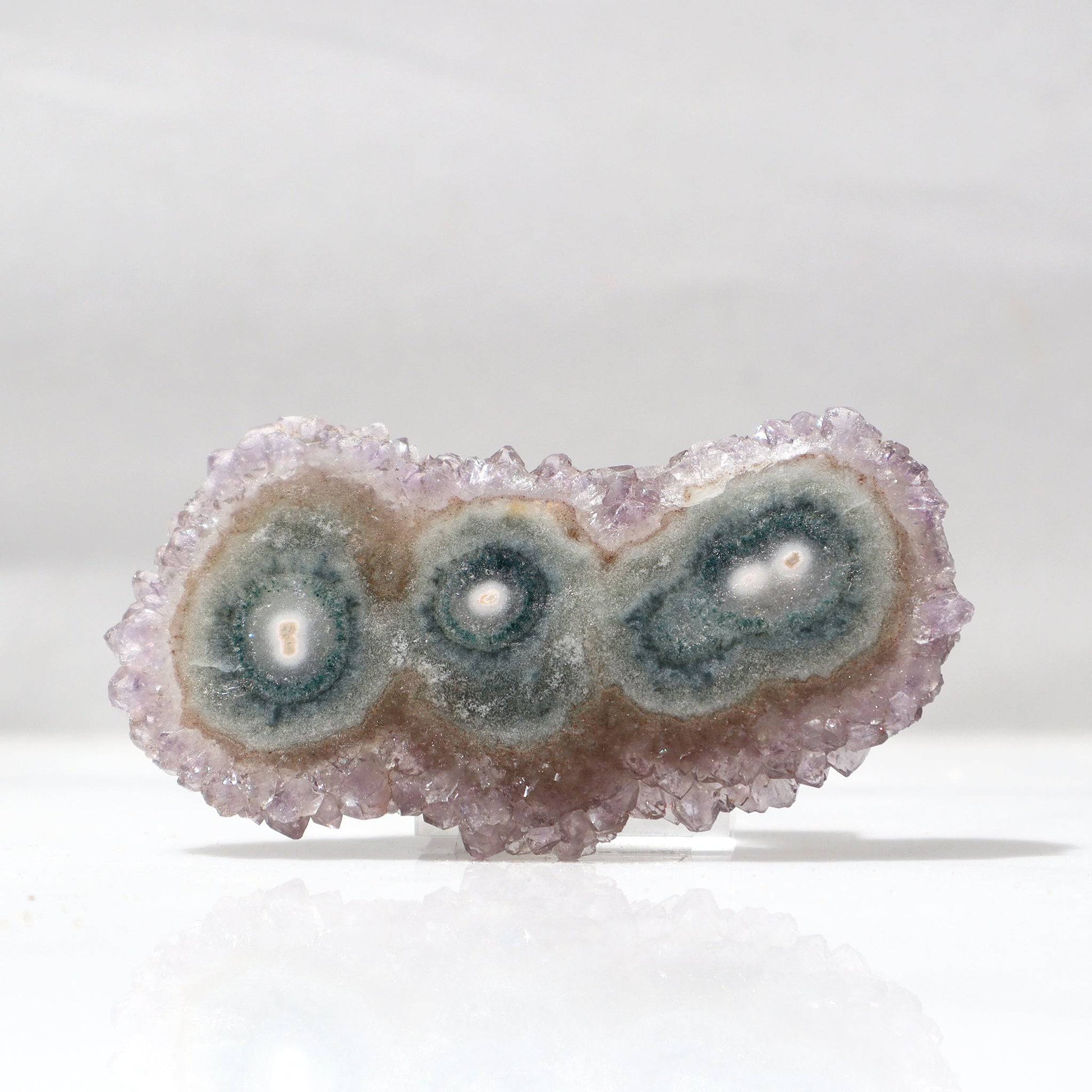 This particular stalactite slice resembles a playful caterpillar with a triple center of dainty green agate with bordering lilac crystals as a complete composition of harmonic mineral balance and beauty.   