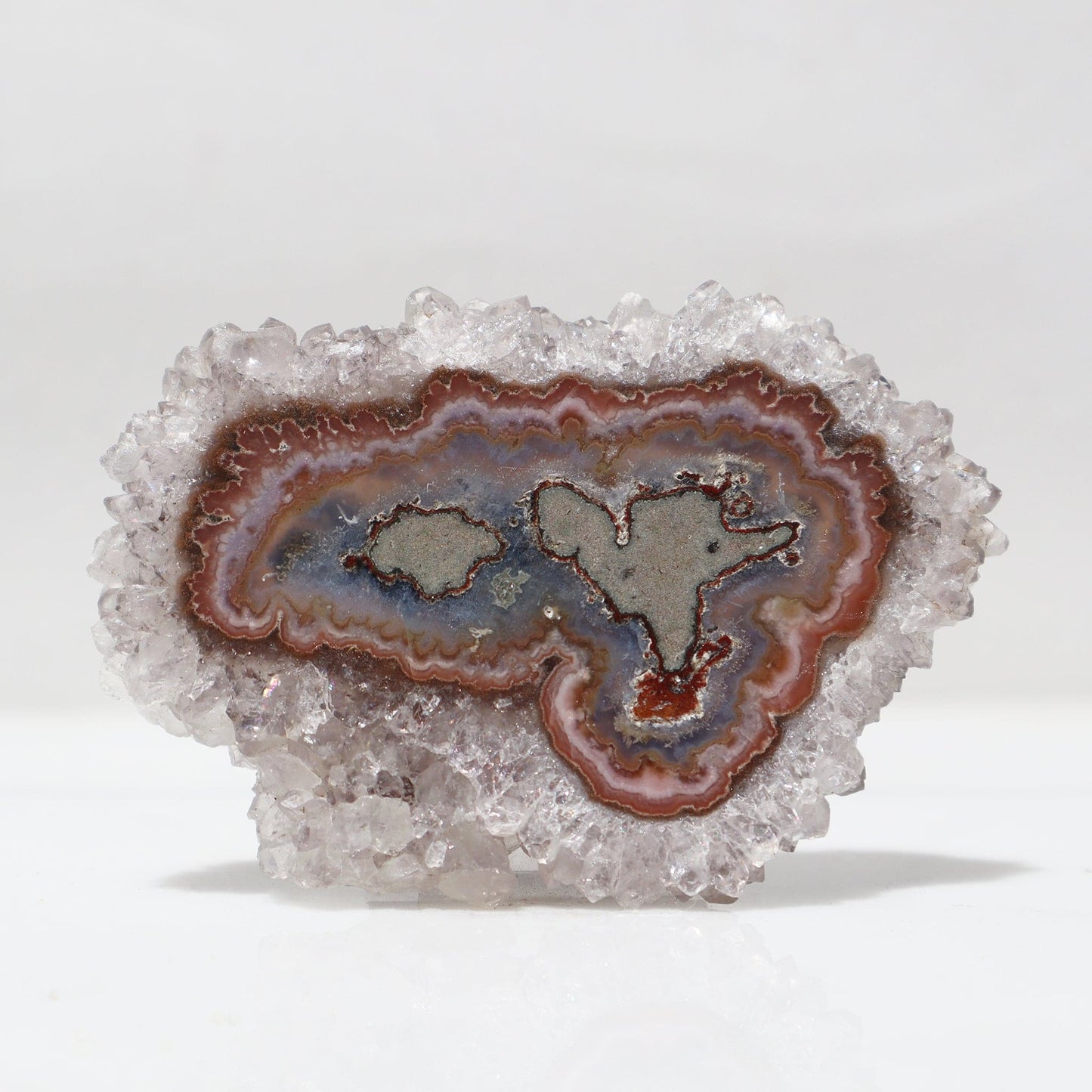 Undulating edge and amusing earthy tones amethyst stalactite slice. A sizable band of white quartz crystals frames the beautiful nature-made minerals design of blue and brown jasper. Also visible is a band of pink jasper and a hint of red hematite. 