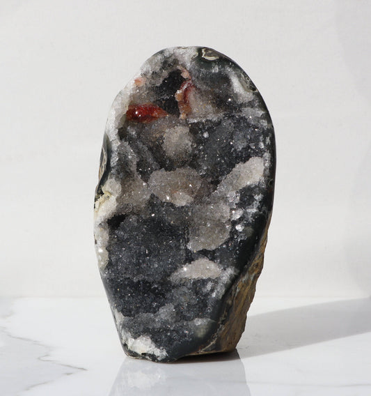 Amethyst of atypical steel color, with patches of white quartz, a section of crystalized red hematite is visible, as well as a band of grey quartz which contrasts with yellow-orangey back.
