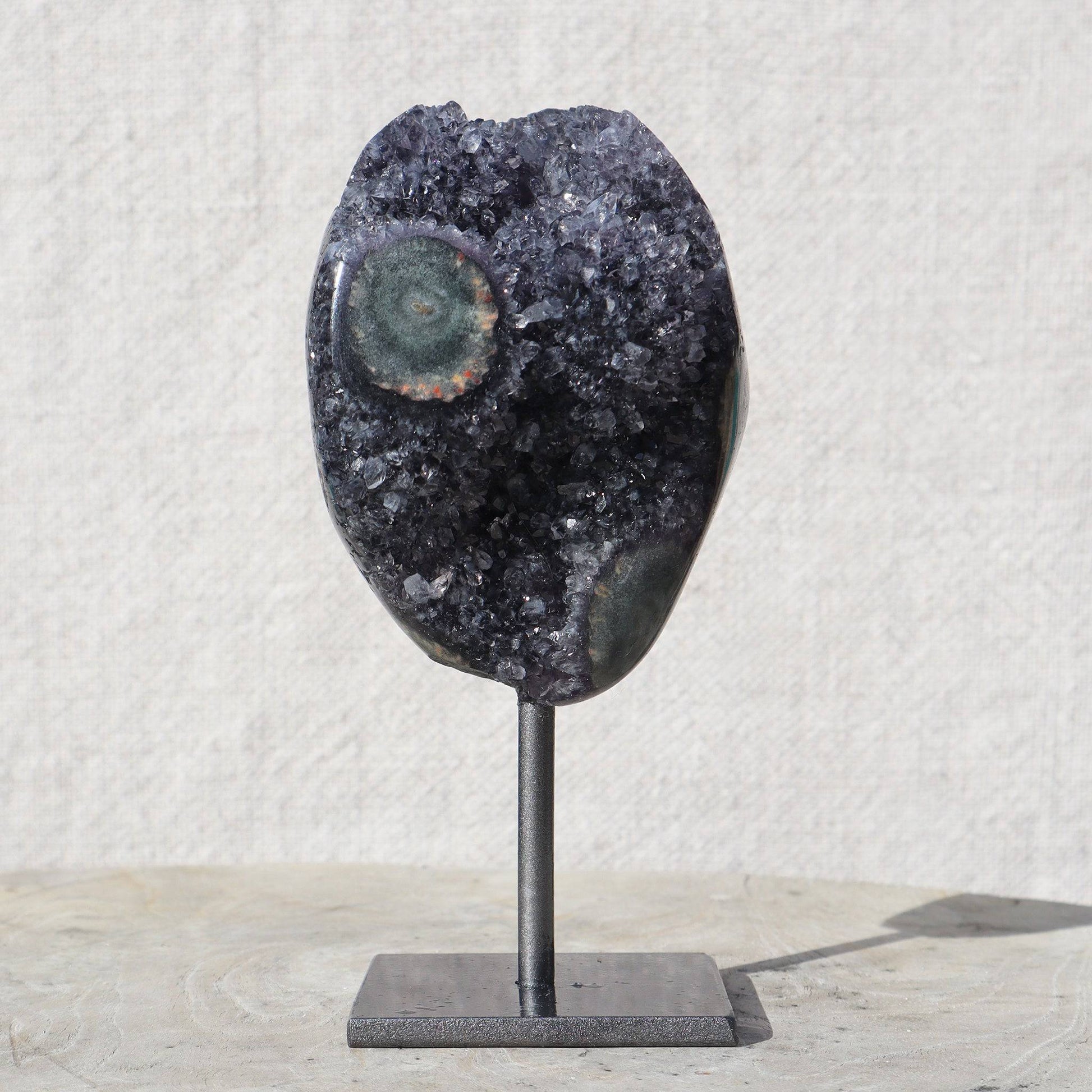 Appealing mounted amethyst of lite charcoal color with a tint of purple quartz crystals with exceptional detail of a colorful green agate cut stalactite. The polished back elevates the aesthetics of this small piece belonging to your desk or bedside.