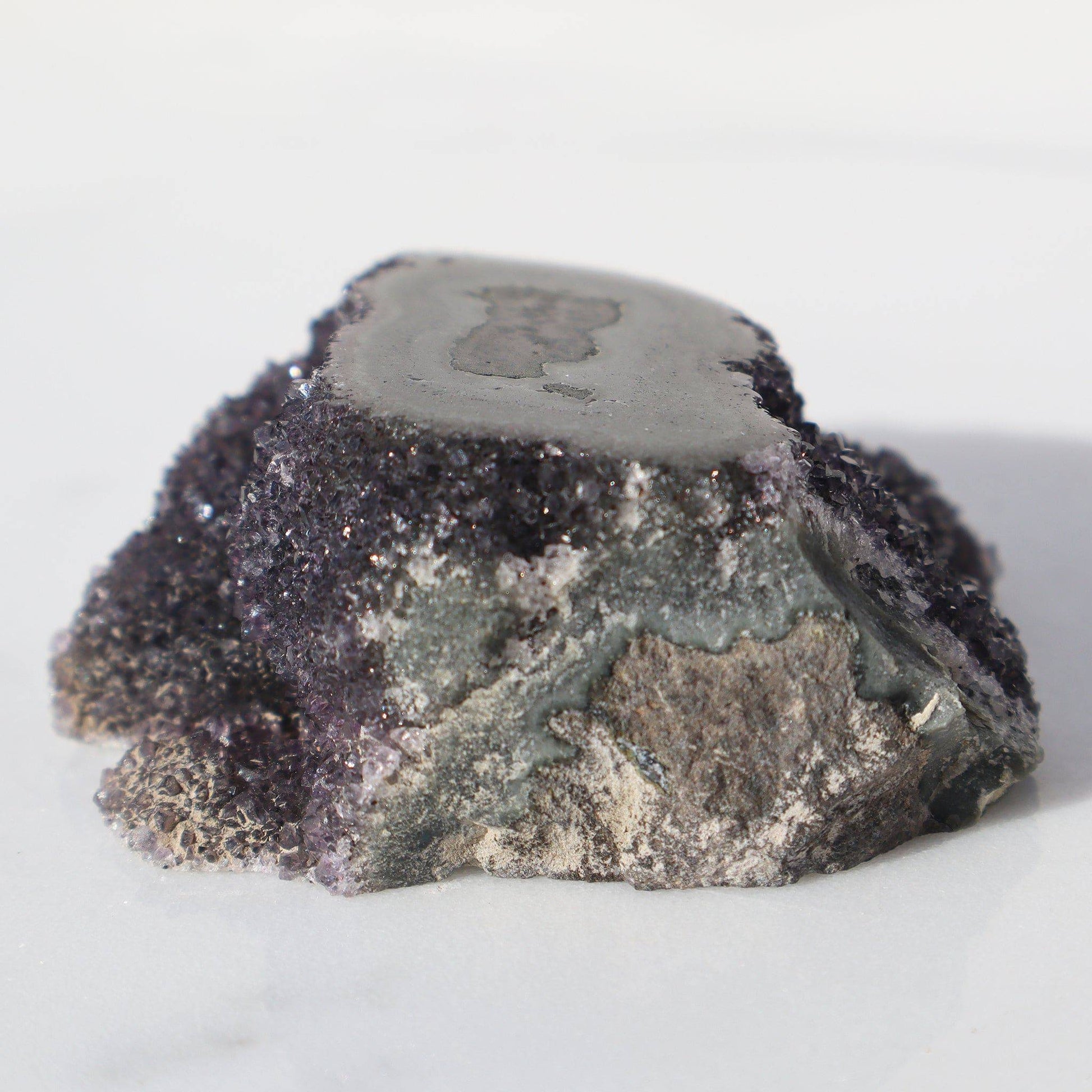 Small volcano-resembling cluster formation. Surrounded by charcoal-purple color micro crystals exposing a cut stalactite on its top. Visible green celadonite. Unpolished basalt for a very raw and primeval look. 